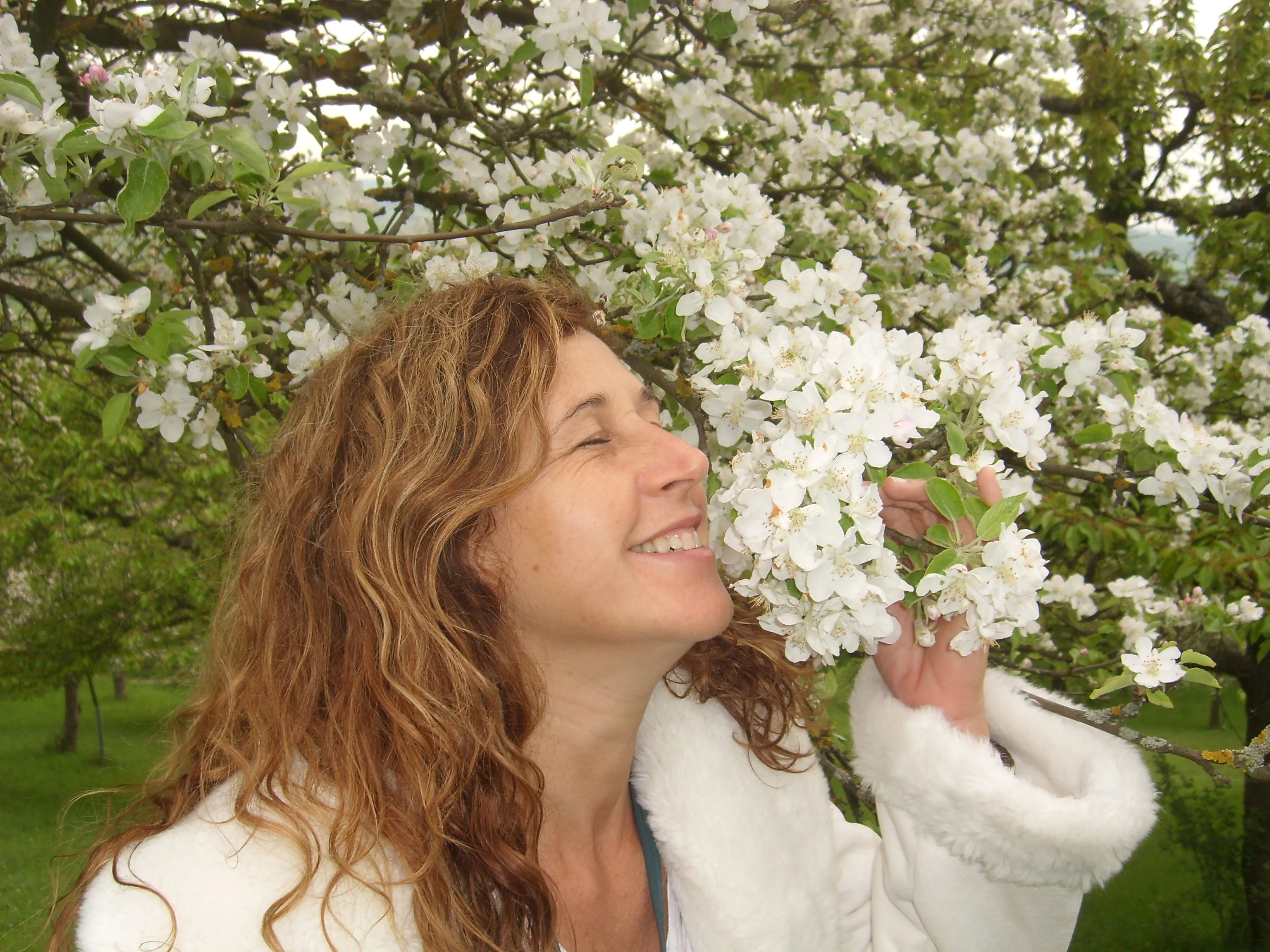 Mônica Oliveira sorrindo de olhos fechados, envolta em flores de macieira